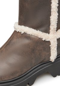 Stivale in pelle marrone con finitura texturizzata, bordo in lana bianca e suola in gomma nera robusta con modelli di trazione.