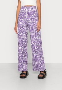 Calças largas de padrão zebra em roxo e branco com cintura alta, apresentando um fecho na frente e dois bolsos laterais, feitas de tecido leve.