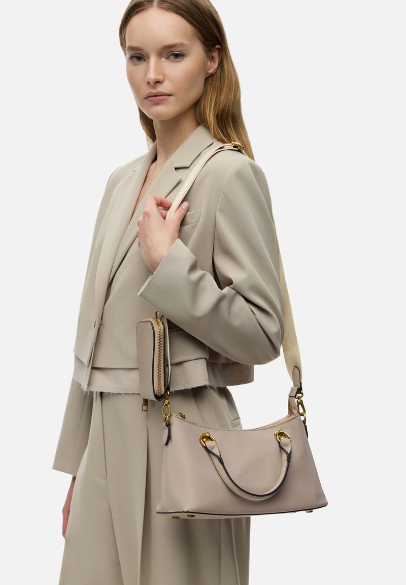 Borsa a tracolla in pelle beige con finiture dorate, forma arrotondata, manico corto e tracolla lunga. Accompagnata da un piccolo portafoglio coordinato.