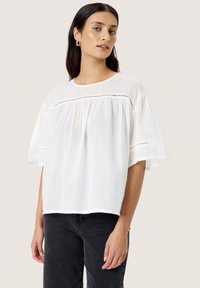 Weiße, locker sitzende Bluse mit kurzen Ärmeln aus strukturiertem Stoff und leicht gerafftem Design. Sie verfügt über ein dezentes Nähmuster entlang des Halsausschnitts.