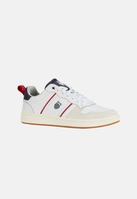 Sneaker bianco con strisce rosse e blu navy, dettagli in suede, suola in gomma e logo sul lato. Inclusi lacci e un anello sul tallone.