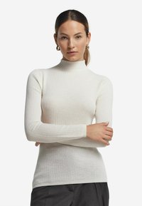 Ribbade vita polotröja gjord av stickat tyg, med långa ärmar och en figurnära design med hög krage.