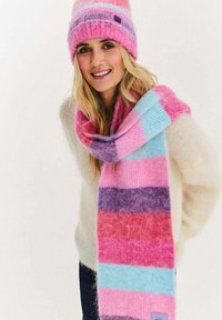 Dziany szalik w różowe, fioletowe i niebieskie paski; miękka tekstura z lekko puszystym wykończeniem. Dopasowany do niego jest czapka w pasy.