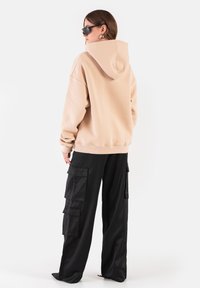 Beżowa bluza z kapturem, luźny krój, ściągacze przy mankietach, w połączeniu z czarnymi spodniami cargo z wieloma kieszeniami i luźnym fasonem.