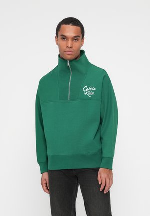 Felpa verde con colletto alto e chiusura a metà zip. Presenta un logo bianco sul petto. Realizzata in tessuto testurizzato.