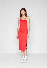 Robe midi rouge avec des fines bretelles, design moulant, fentes latérales, en tissu doux, portée avec des baskets blanches et des chaussettes de cheville.