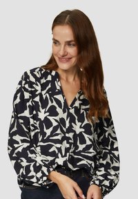 Schwarz-weiße gemusterte Bluse mit lockerer Passform, tiefem V-Ausschnitt und gerafften langen Ärmeln. Strukturiertes Material, geeignet für legere Anlässe.