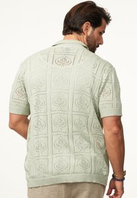 Hellgrünes, gestricktes kurzärmliges Shirt mit einem geometrischen Ausschnitt-Muster, strukturierter Stoff und einem geraden Saum mit gerippten Kanten.