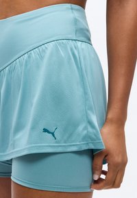 Κοντινό πλάνο ενός ατόμου που φοράει αθλητικό σορτς σε ανοιχτό μπλε με στρώσεις, με το λογότυπο Puma και το χέρι ξεκουράζεται δίπλα στον μηρό.