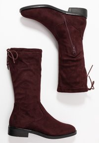 Bottes hauteur genou en daim bordeaux avec une fermeture éclair latérale et un lacet décoratif en haut. Semelle plate robuste avec un petit talon et texture lisse.