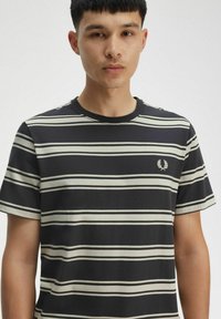 T-shirt a righe nere con strisce bianche orizzontali, collo a giro, e un piccolo emblema ricamato sul lato sinistro del petto. Maniche corte.