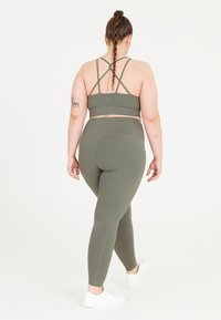Olivgrön sportbh med korsade axelremmar, i kombination med matchande högmidjade leggings, båda tillverkade av stretchigt, mjukt tyg.