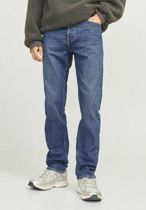 Jeans de mezclilla azul con un corte recto, que presentan un ligero desgaste y costuras en contraste. Combinados con un suéter de felpa gris y zapatillas plateadas.