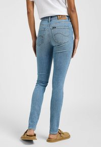 Jeans de denim azul ajustados con una cintura alta, que presentan un parche de cuero de la marca, bolsillos traseros y costuras a contraste.