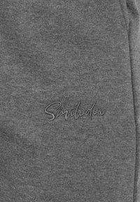 Grijze stof met een zachte textuur met een geborduurd "Smilodex"-logo in een contrasterende kleur. Geen duidelijke patronen of hardware zichtbaar.