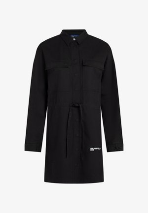 Fekete farmeringruha gombos elejével, hosszú ujjú, két mellzsebbel és húzózsinórral a derékon. Az alján logó található.