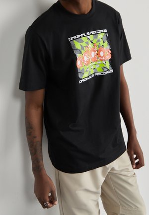 T-shirt en coton noir avec un imprimé graphique coloré comprenant du texte, incluant des éléments orange et verts, sur un fond à carreaux.