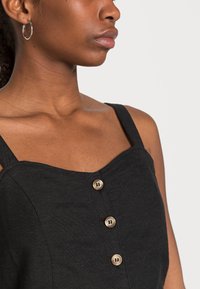 Vestido de linho preto com alças largas, apresentando um decote coração e três botões funcionais em castanho claro ao longo da frente.