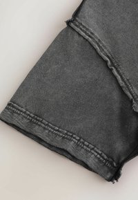 Détails de l'ourlet et de la couture d'un tissu en denim gris foncé plié sur une surface claire, montrant une double couture et un léger effilochage aux bords.