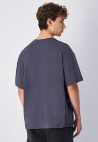 Szara, oversize koszulka z miękkiej bawełny, z okrągłym dekoltem i krótkimi rękawami, o luźnym kroju i bocznymi rozcięciami dla większej wygody.