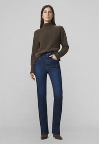 Rjav visok ovratnik pletena majica, kombinirana z temno modrimi kavbojkami z ravnimi nogavicami. Obleka ima preprost, priložnostni dizajn z minimalnimi podrobnostmi.