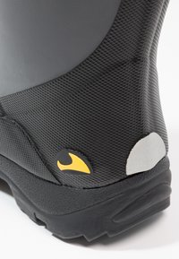 Bota preta de borracha com acabamento texturizado, apresentando um detalhe em amarelo e cinza no calcanhar. Sola robusta com um padrão antiderrapante.