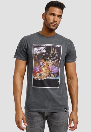 Grafisk t-shirt i mörkgrå bomull, med en färgglad filmaffischdesign. Utmärkande text inkluderar "IMPERIO CONTRA-ATAQUE." Kort ärm.