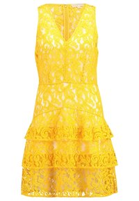 Robe sans manches en dentelle jaune avec col en V, jupe à volants superposés et fermeture éclair visible dans le dos.