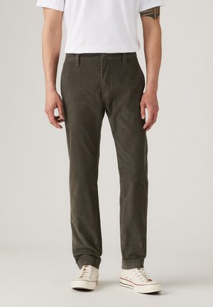 Olive green corduroy pants with a straight cut, featuring front pockets and a button closure, paired with white sneakers.