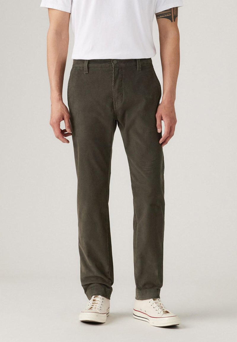 Olive green corduroy pants with a straight cut, featuring front pockets and a button closure, paired with white sneakers.