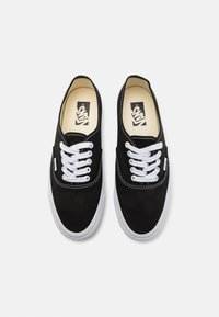 Black canvas sneakers with white laces, rubber soles, and contrasting white stitching. Branding visible on the insole. Classic design.