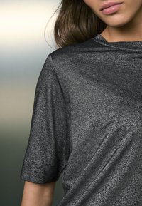 Kovovo čierna krátky rukáv košeľa s hladkou, lesklou textúrou a zaobleným výstrihom, s jemným leskom a voľným strihom.