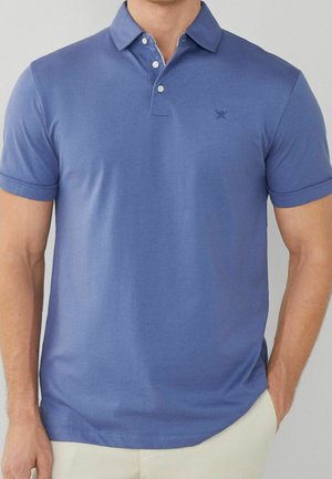 Man wearing a short-sleeve, blue polo shirt with a two-button collar and small embroidered logo on the chest.
