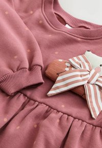 Zacht roze kinderjurk met kleine oranje stippen, geribde manchetten en een vastgenaaide stoffen teddybeer met een gestreepte strik.