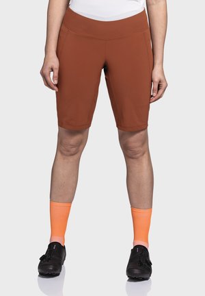 Braune Fahrradhosen mit enganliegendem Design, glatter Textur und elastischem Bund. Kombination mit knielangen orangefarbenen Socken und schwarzen Schuhen.