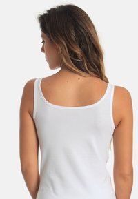 White tank top with thin straps, featuring a scoop back design. Smooth texture without any patterns or embellishments.