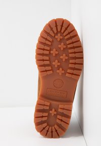 Semelle d'une botte Timberland beige avec un motif de relief profond comprenant des croix et des rainures pour l'adhérence, sur fond blanc.