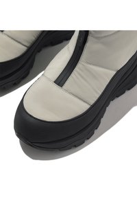 Lichtgrijze gevoerde schoenen met een zwarte rubberen zool, voorzien van een ritsluiting en textuurelementen langs de randen voor extra grip.