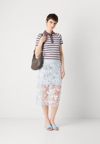 Polo rayé en violet et blanc, associé à une jupe légère en tulle bleu clair brodée de fleurs. Sandales bleues décontractées et sac marron.
