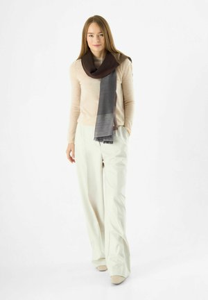 Écharpe marron et grise en tissu doux, drapée de manière décontractée. Texture lisse avec des bords à franges. Associée à un pantalon et un haut de couleur claire.