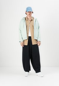 Light mint oversized hoodie, tan button-up shirt, black wide-leg pants, white sneakers, and a light blue cap with a logo.