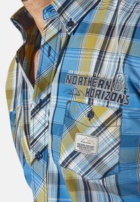 Short-sleeve checkered shirt featuring blue, green, and beige plaid patterns, with a chest pocket and logo embroidery.