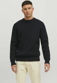 Maglione a coste di un navy scuro con scollatura rotonda e maniche lunghe, caratterizzato da una superficie testurizzata e orlo aderente. Abbinato a pantaloni chiari.