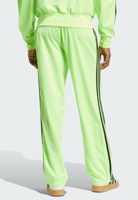 Neon green athletic pants made of smooth polyester, featuring black side stripes and a relaxed fit, with elastic cuffs at the ankles.