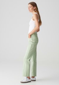 Pantaloni verde chiaro a vita alta con design a gamba dritta. Realizzati in cotone con una finitura pulita e tasche. Abbinati a sneakers bianche.