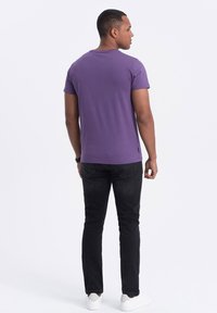 T-shirt viola fitted da uomo con maniche corte, scollatura tonda e texture liscia. Indossato con jeans neri e sneakers bianche.