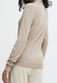 Maglione beige a collo alto realizzato in morbido tessuto a maglia, con maniche lunghe e orlo a costine, mostrato da dietro con una vestibilità comoda.