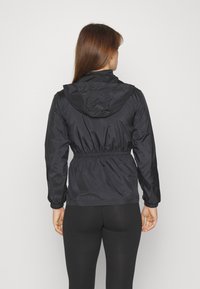 Sort letvægtsjakke med hætte, elastisk talje og indsnørede manchetter. Glat tekstur og minimalistisk design. Bagfra set.