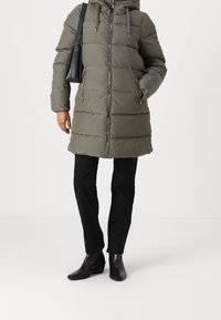 Parka acolchada verde oliva con cierre de cremallera en la parte delantera, capucha y cordón ajustable. Cuenta con dos bolsillos laterales y un diseño hasta la rodilla.