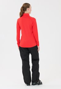 Rode longsleeve top met hoge kraag en aansluitend design, gecombineerd met zwarte, loszittende broek. Matte textuur; sportieve uitstraling.